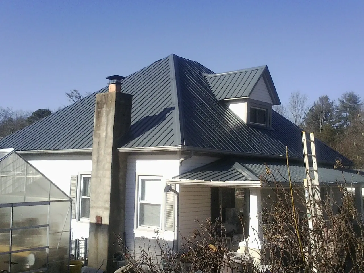 Dark blue standing seam metal roof on a white farmhouse with dormer in Melrose Park