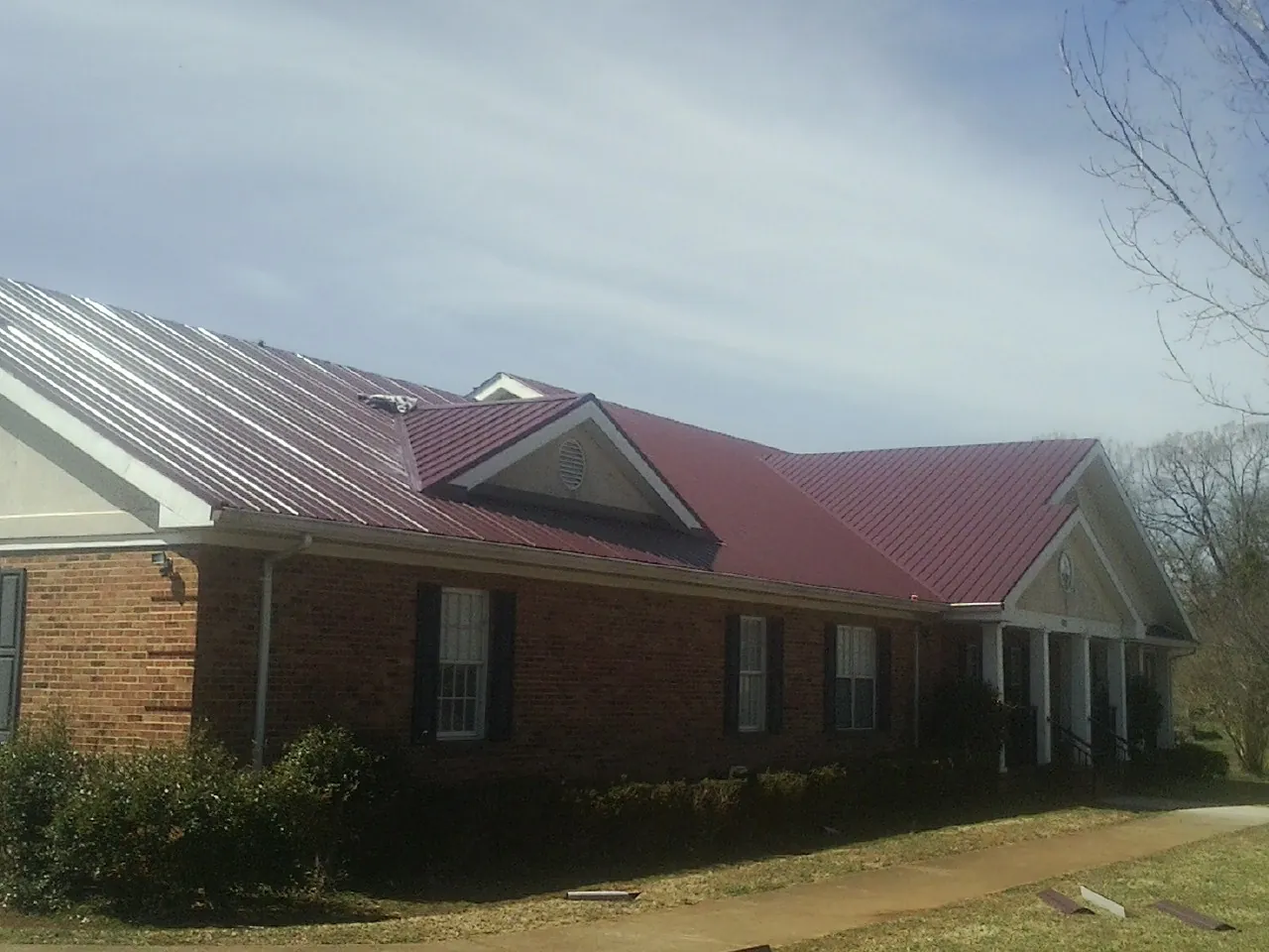 Red metal roof with gabled entries on a long brick building, from a Hail Damage Roof Repair job in Melrose Park