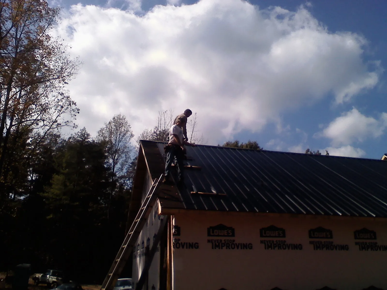 Roofer fastening dark metal panels high against a cloudy sky, from a Roof Inspection job in Melrose Park