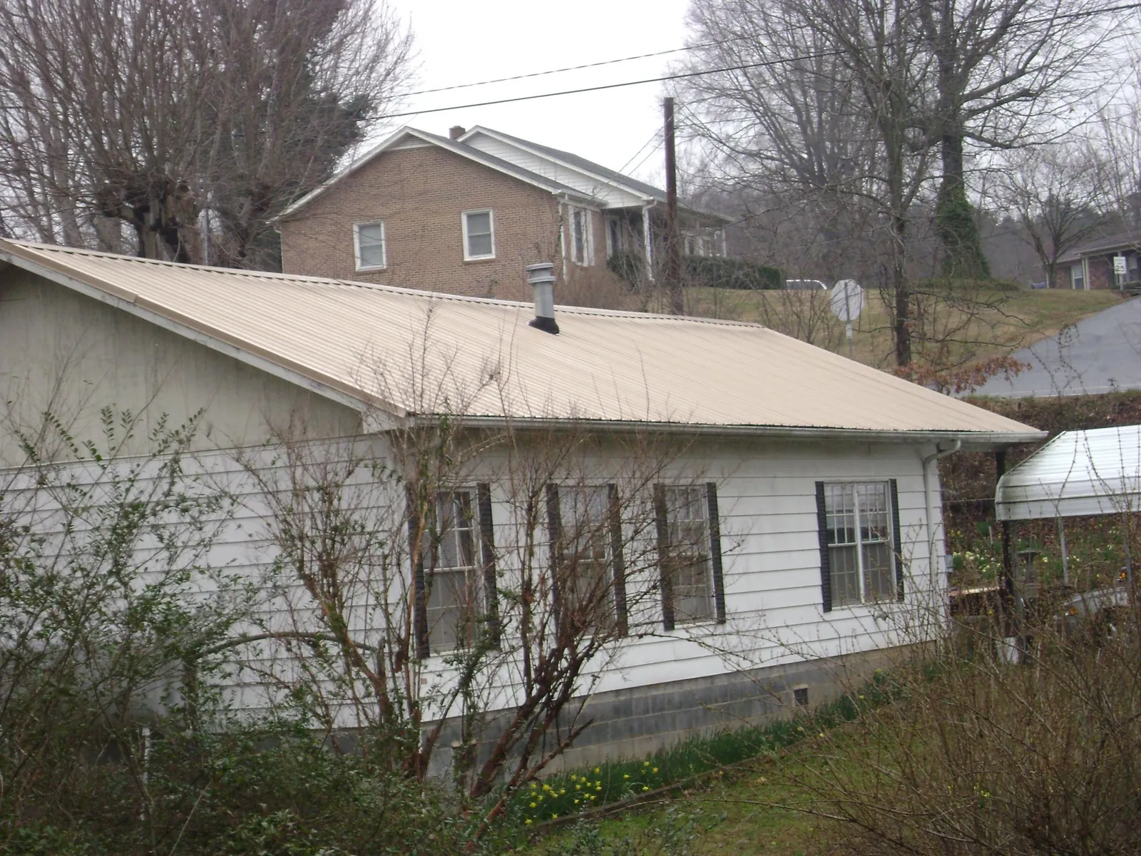 Tan metal roof on a white sided house set into a hillside — Commercial Roofing by Roofing Brothers in Melrose Park