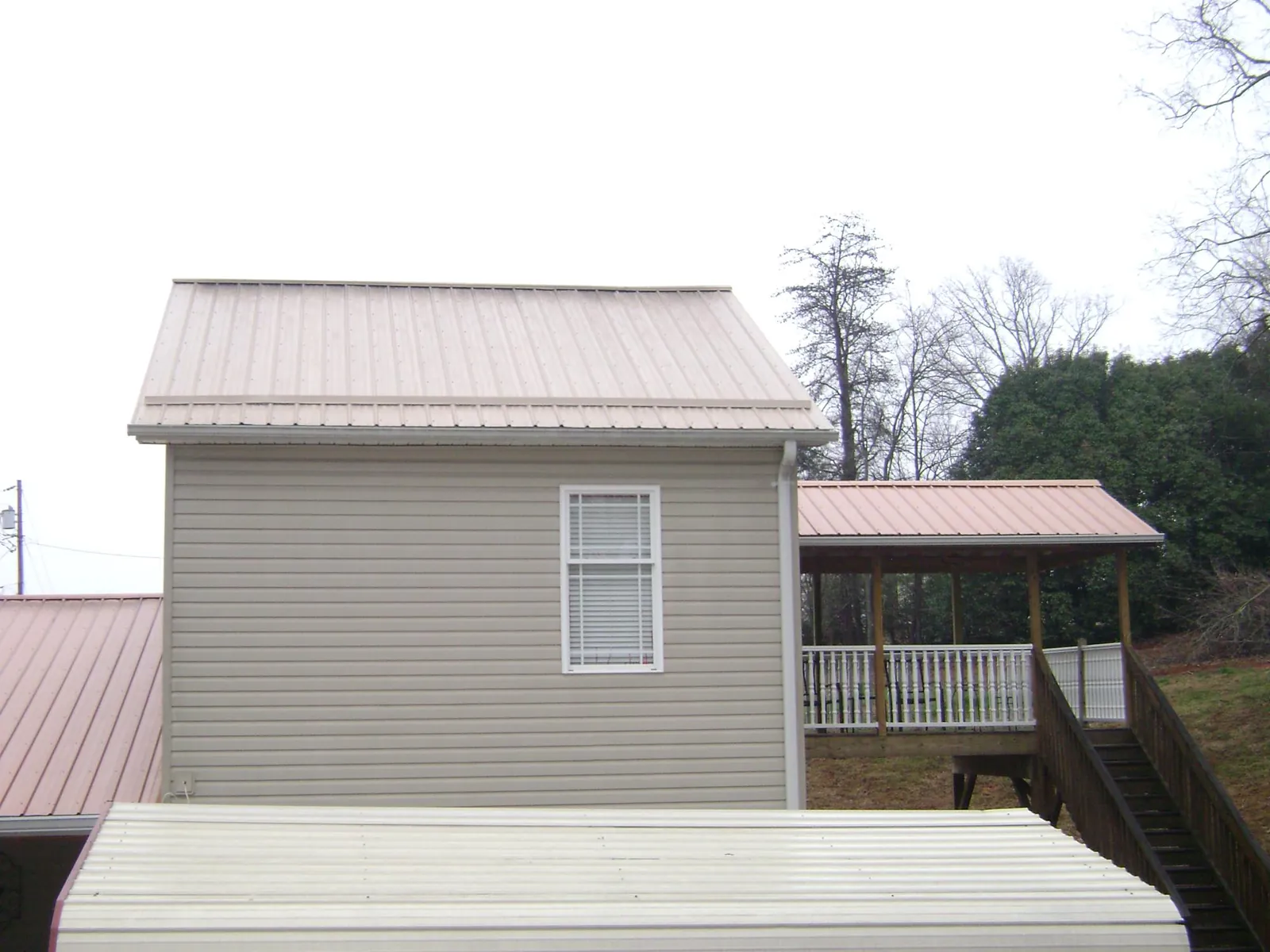 Tan metal roofs on a two story addition and attached porch, from a Roof Replacement job in Melrose Park